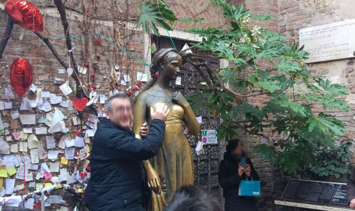 Homem tocando o peito da estátua de Julieta em na Casa de Julieta, em Verona
