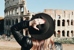 Mulher de costas, com a mão segurando seu chapéu, de frente ao Coliseu, em Roma, na Itália