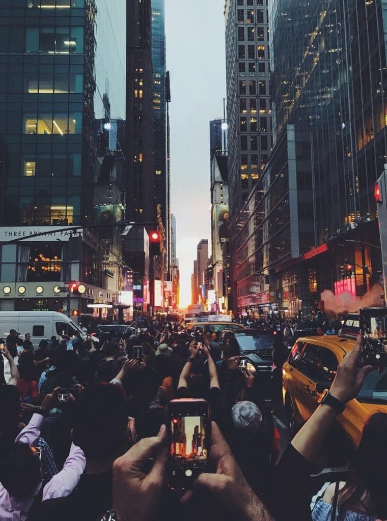 Foto de uma rua lotada em Nova York, no por do sol, com muitos celulares tirando fotos ao mesmo tempo