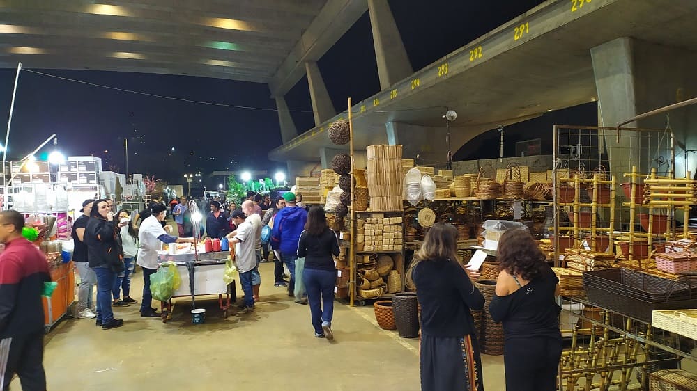 Feira de Flores do CEAGESP, com um carrinho no centro onde se vendem café e, dos lados, prateleiras com vasos e objetos de paisagismo