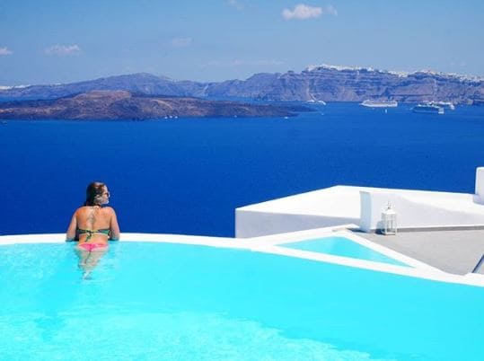 Mulher de costas, na beira da piscina, com vista para o mar em Santorini, na Grécia