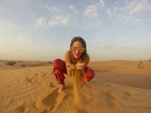 Mulher no deserto em Dubai, agachada, segurando um punhado de areia