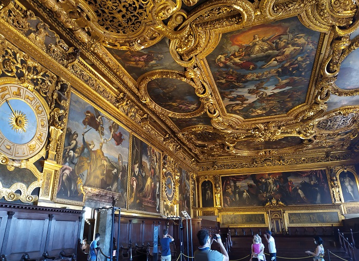 Foto aberta de uma sala com afrescos no teto e nas paredes com adornos dourados no Palazzo Ducale, em Veneza