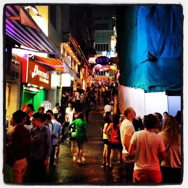 Foto à noite, numa rua estreita cheia de pessoas em Hong Kong