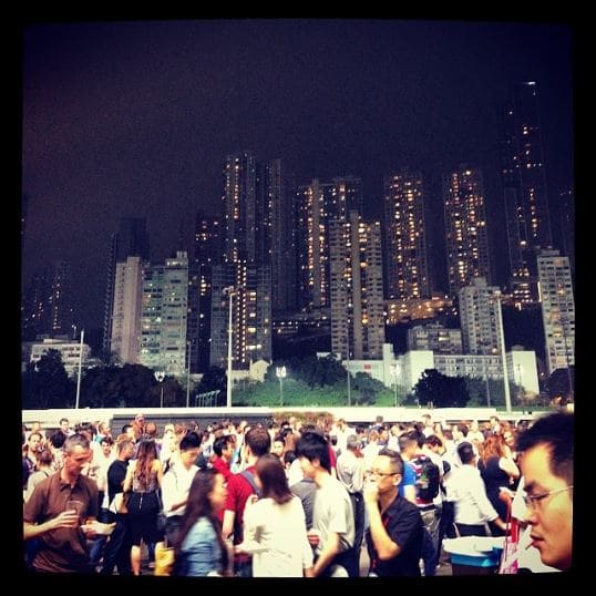 Foto tirada no Jockey em Hong Kong, com pessoas à frente e, no fundo, muitos prédios 