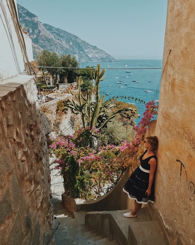 Foto de uma mulher encostada numa parede com o mar ao fundo em Positano, na Itália