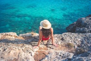 Photo by Jo Kassis: https://www.pexels.com/photo/woman-in-hat-and-red-bikini-sitting-on-rock-near-water-5522434/